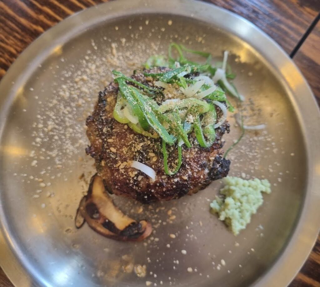  A plate of Don-Jijim, a Korean beef patty topped with green onions and sprinkled with seasoning, served with a side of wasabi.