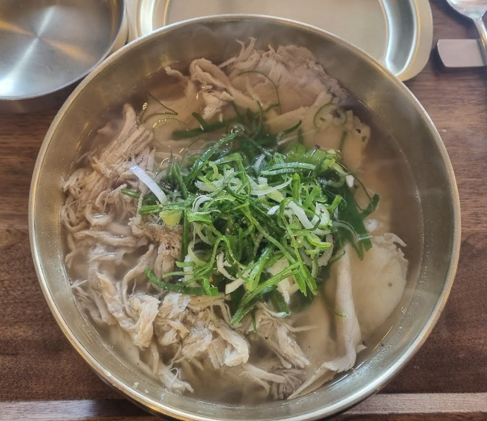 A bowl of Don-Gomtang, a Korean beef soup with shredded meat and green onions, served in a brass bowl.